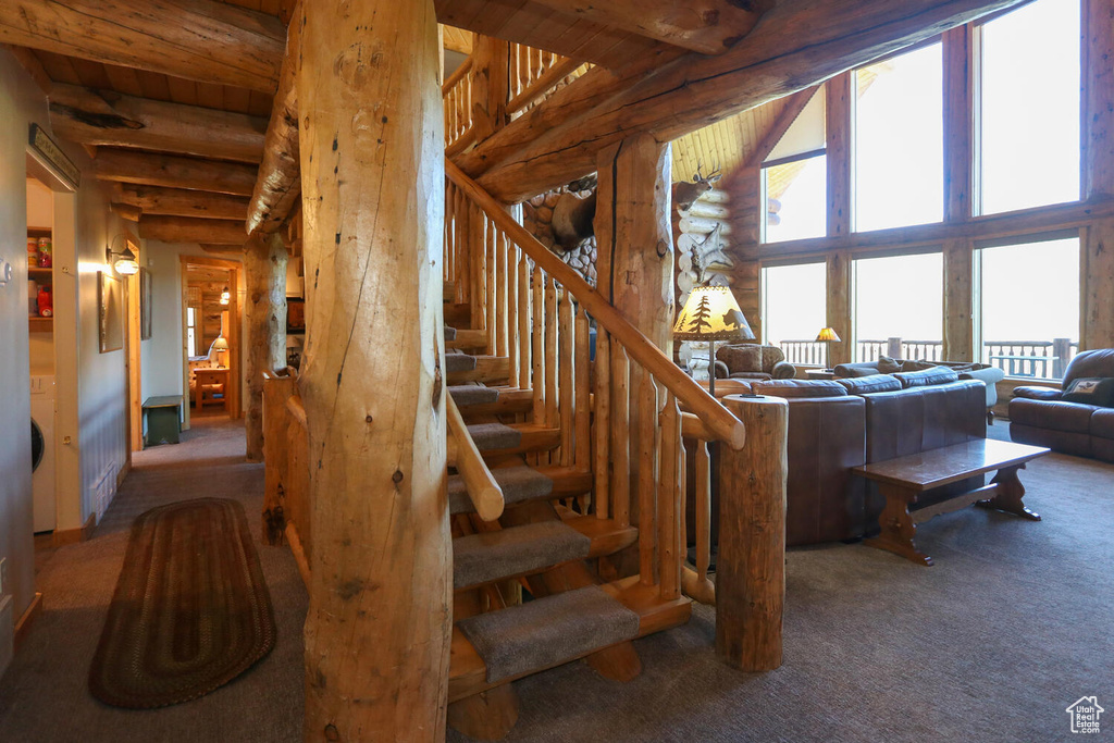 Stairway with beamed ceiling, log walls, and carpet floors