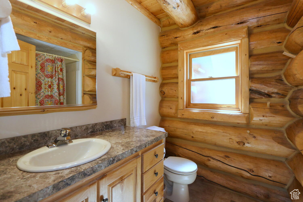 Bathroom featuring wooden ceiling, oversized vanity, toilet, and rustic walls