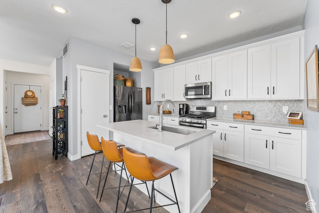 Kitchen featuring white cabinets, sink, dark wood-type flooring, stainless steel appliances, and pendant lighting