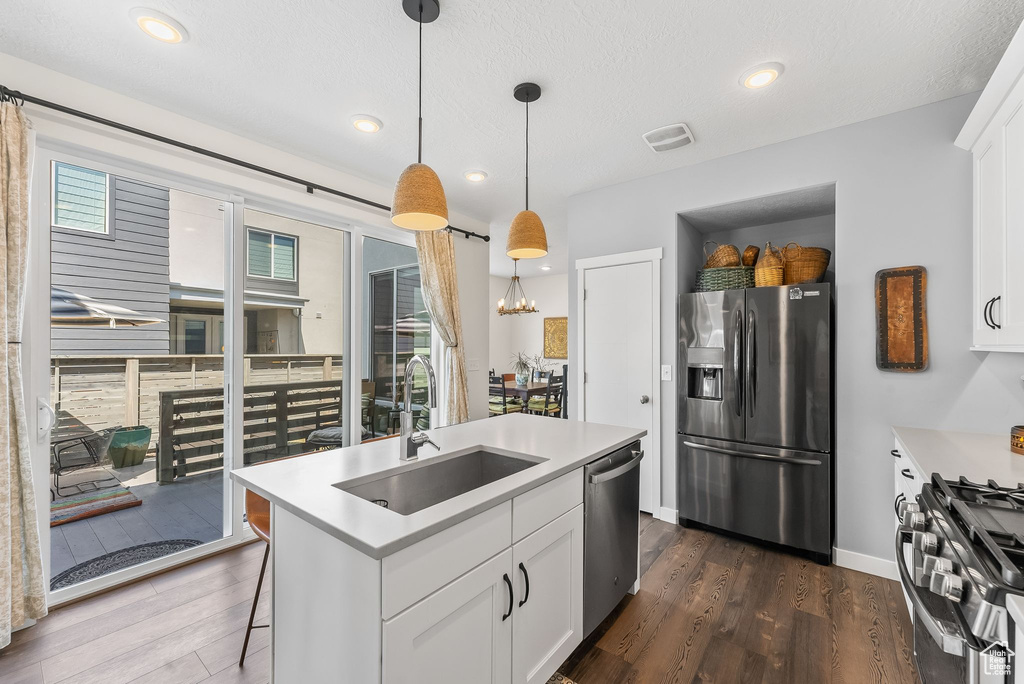 Kitchen featuring appliances with stainless steel finishes, sink, white cabinetry, an island with sink, and pendant lighting