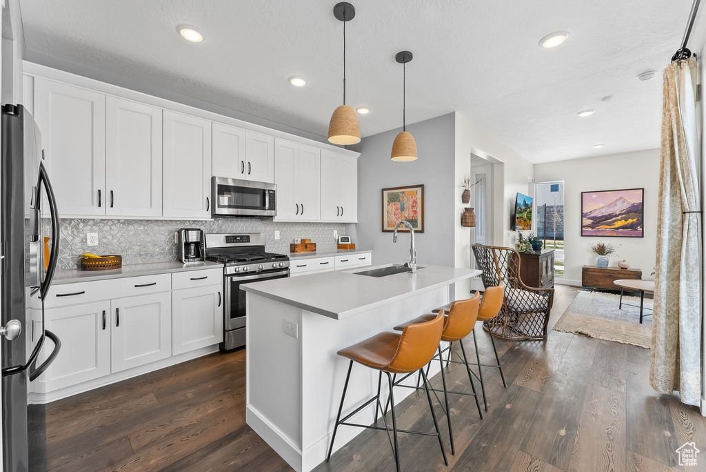 Kitchen with decorative light fixtures, appliances with stainless steel finishes, a center island with sink, dark hardwood / wood-style floors, and white cabinetry