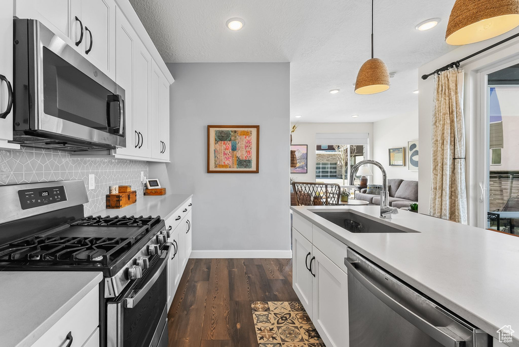 Kitchen featuring white cabinets, sink, tasteful backsplash, stainless steel appliances, and pendant lighting