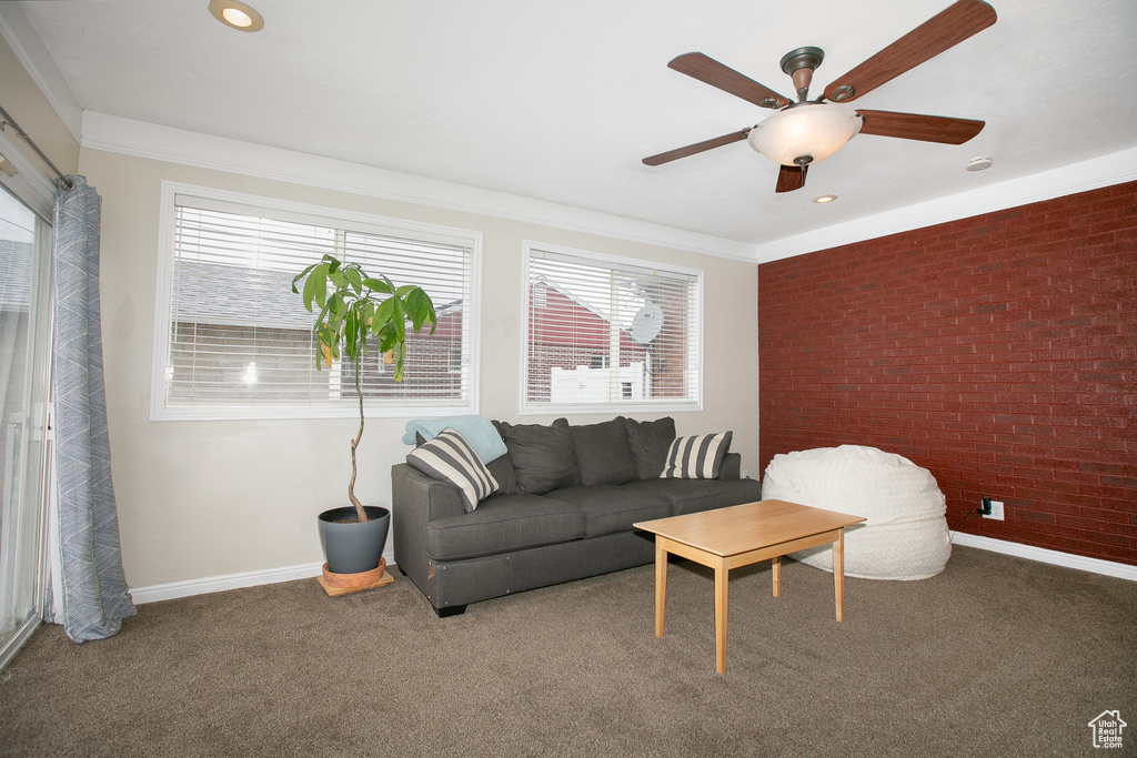 Carpeted living room featuring ceiling fan, brick wall, and ornamental molding