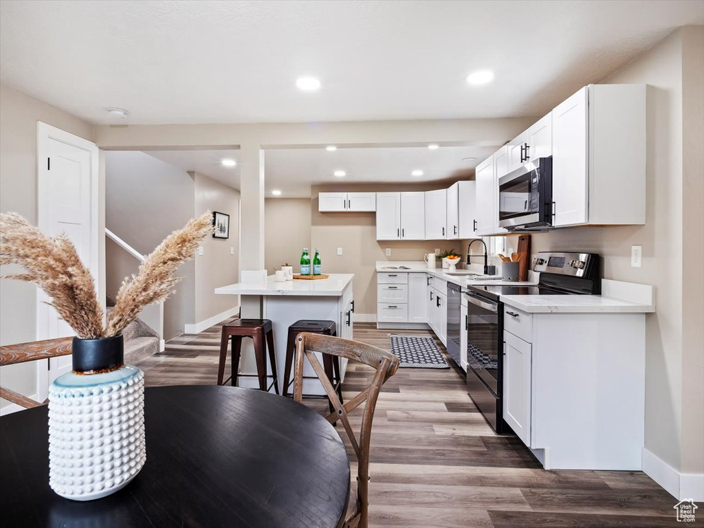 Kitchen featuring appliances with stainless steel finishes, a kitchen island, white cabinets, sink, and wood-type flooring