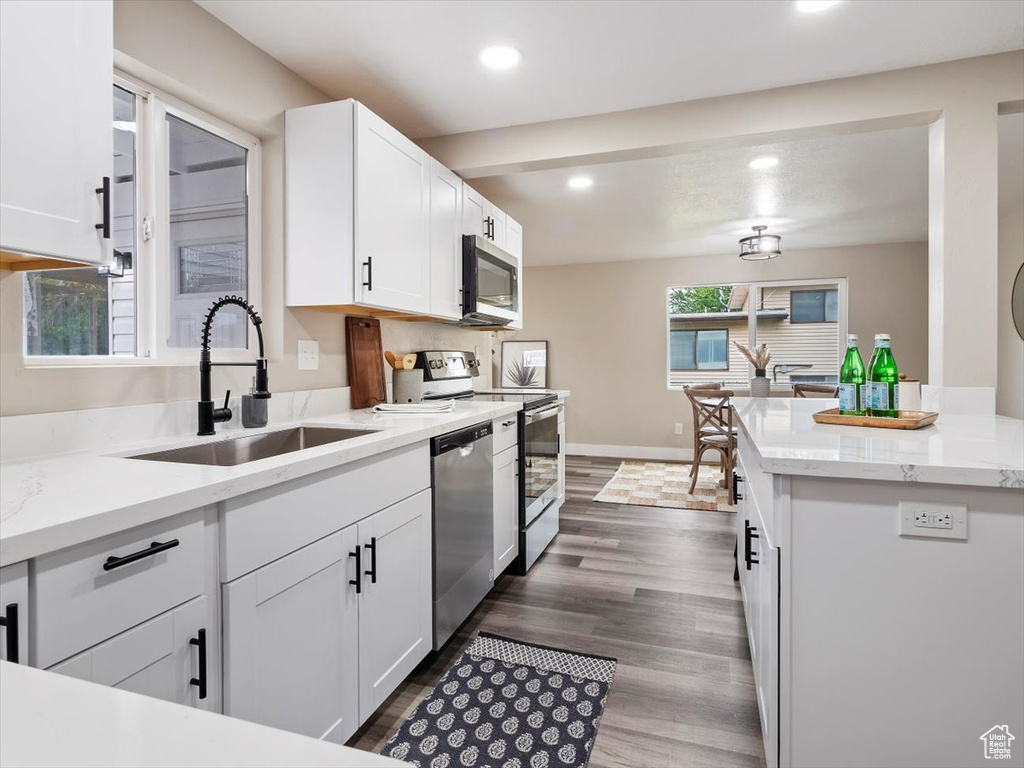 Kitchen featuring appliances with stainless steel finishes, sink, white cabinetry, dark hardwood / wood-style flooring, and light stone countertops