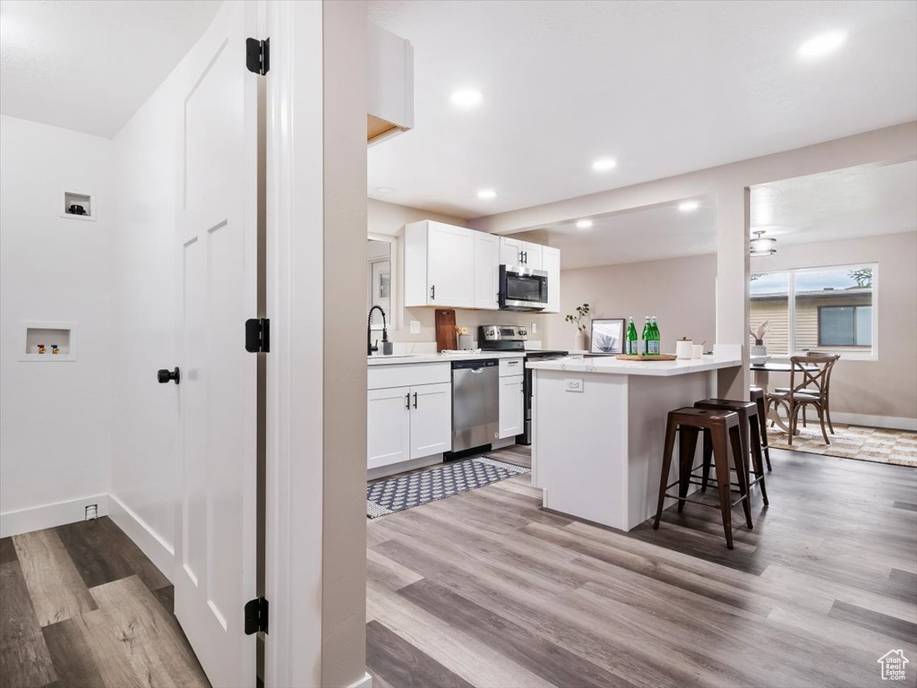 Kitchen with white cabinets, appliances with stainless steel finishes, and light hardwood / wood-style flooring