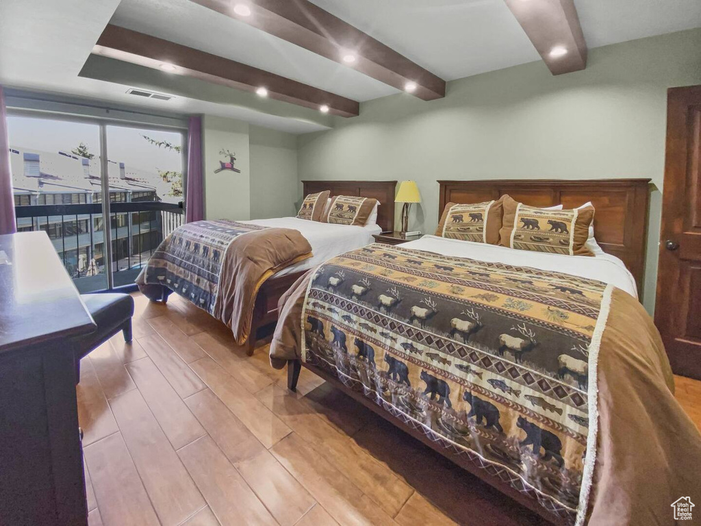 Bedroom with hardwood / wood-style floors, beam ceiling, and access to exterior