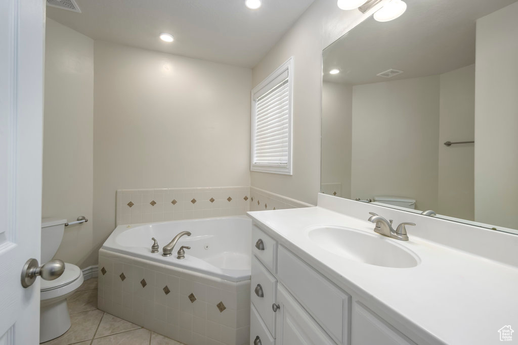 Bathroom featuring tile flooring, tiled tub, vanity, and toilet