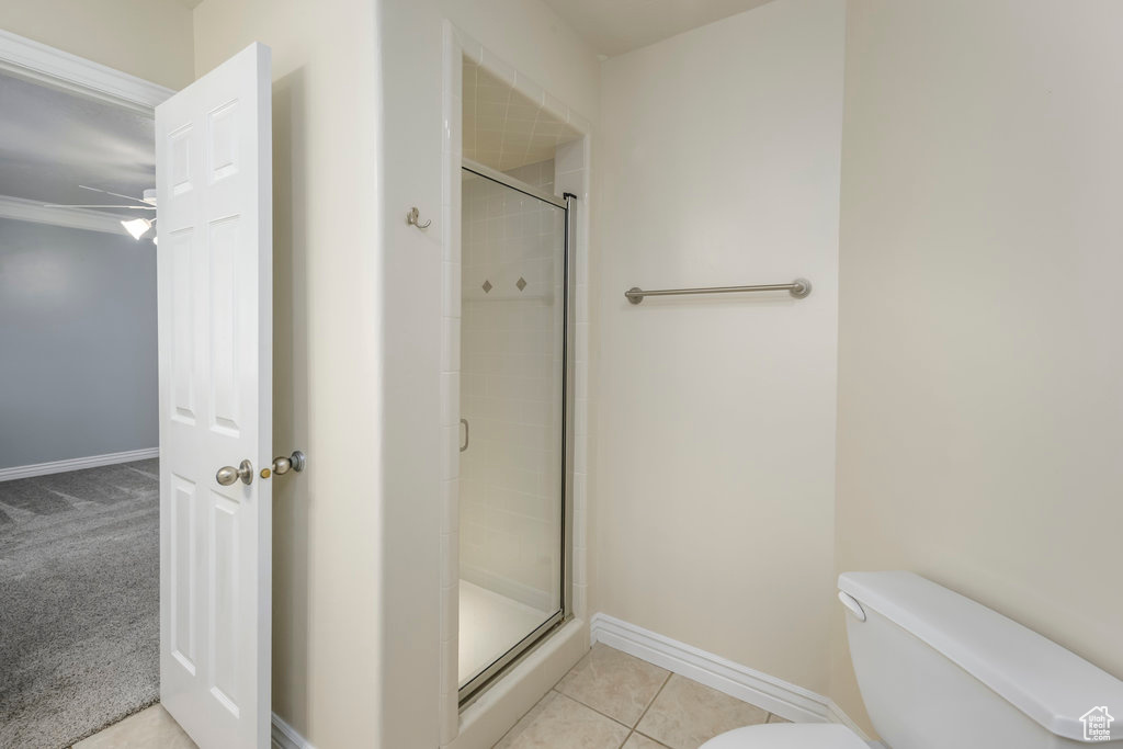 Bathroom featuring a shower with shower door, toilet, tile floors, and ceiling fan