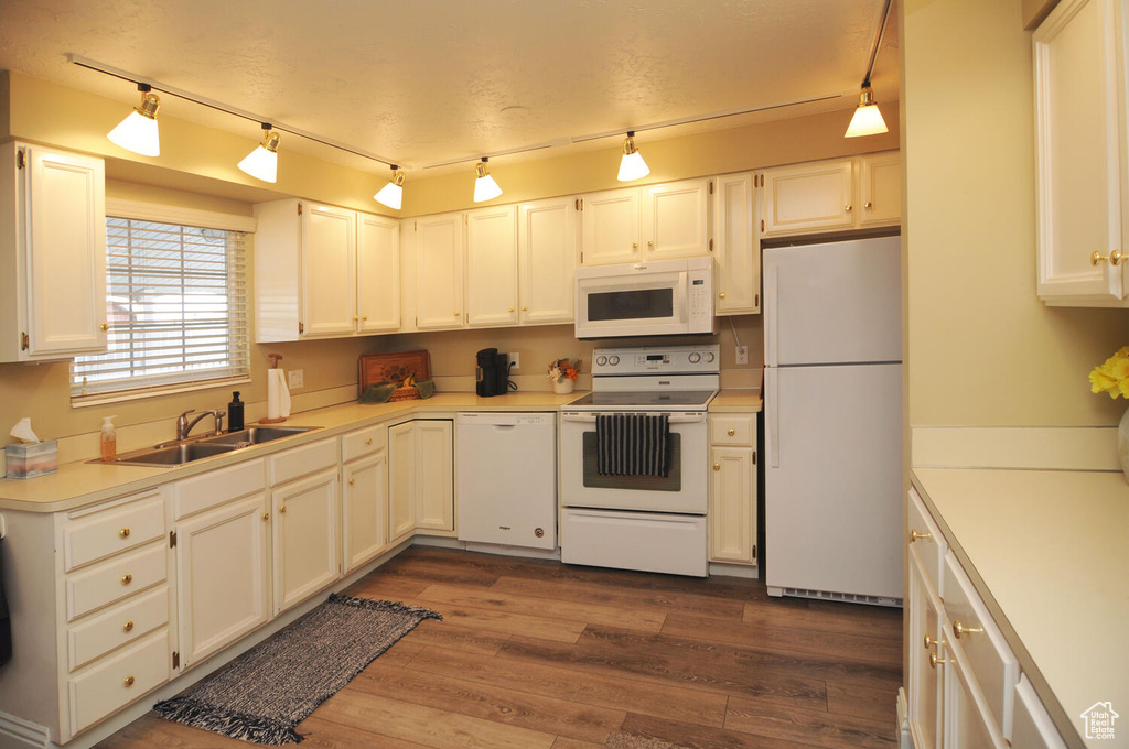 Kitchen with white appliances, dark hardwood / wood-style floors, white cabinetry, rail lighting, and sink