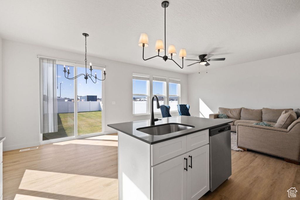 Kitchen featuring light wood-type flooring, dishwasher, sink, white cabinetry, and hanging light fixtures