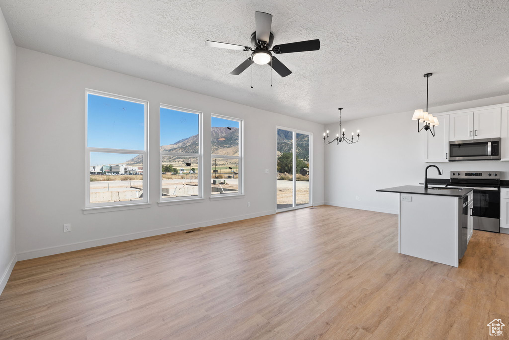 Kitchen featuring decorative light fixtures, a kitchen island with sink, white cabinetry, stainless steel appliances, and light wood-type flooring