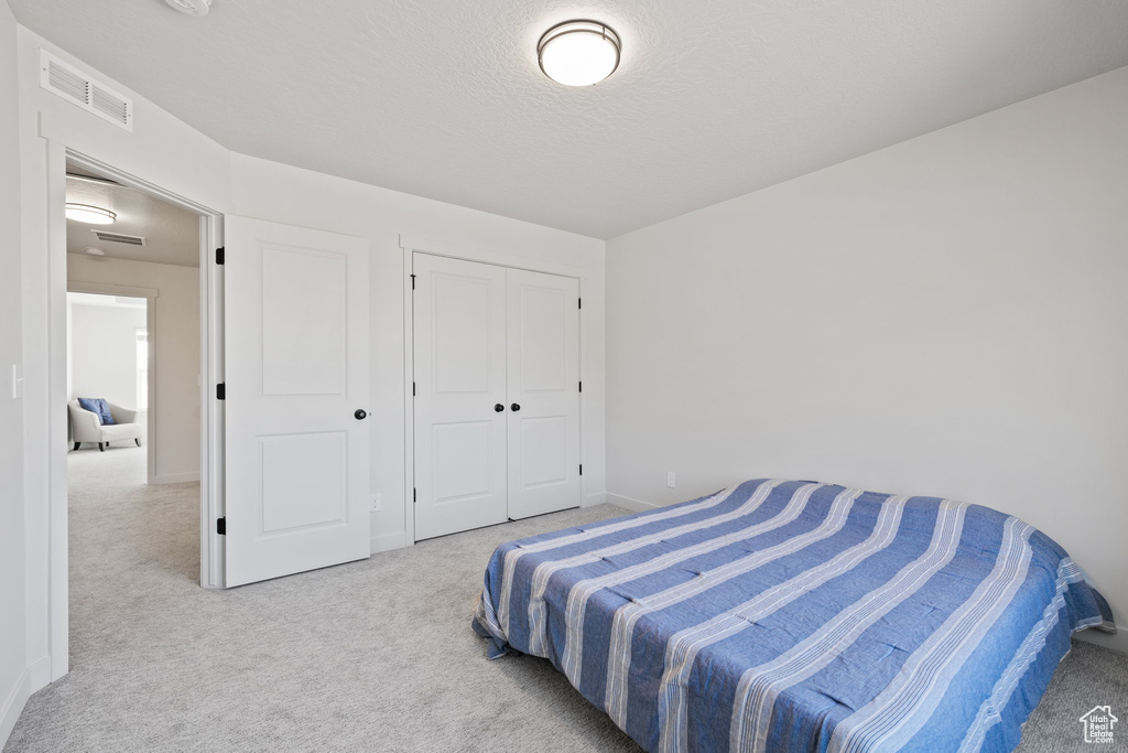 Carpeted bedroom featuring a textured ceiling and a closet