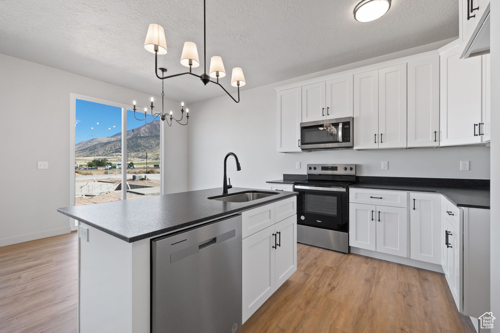 Kitchen featuring white cabinets, sink, stainless steel appliances, and a notable chandelier