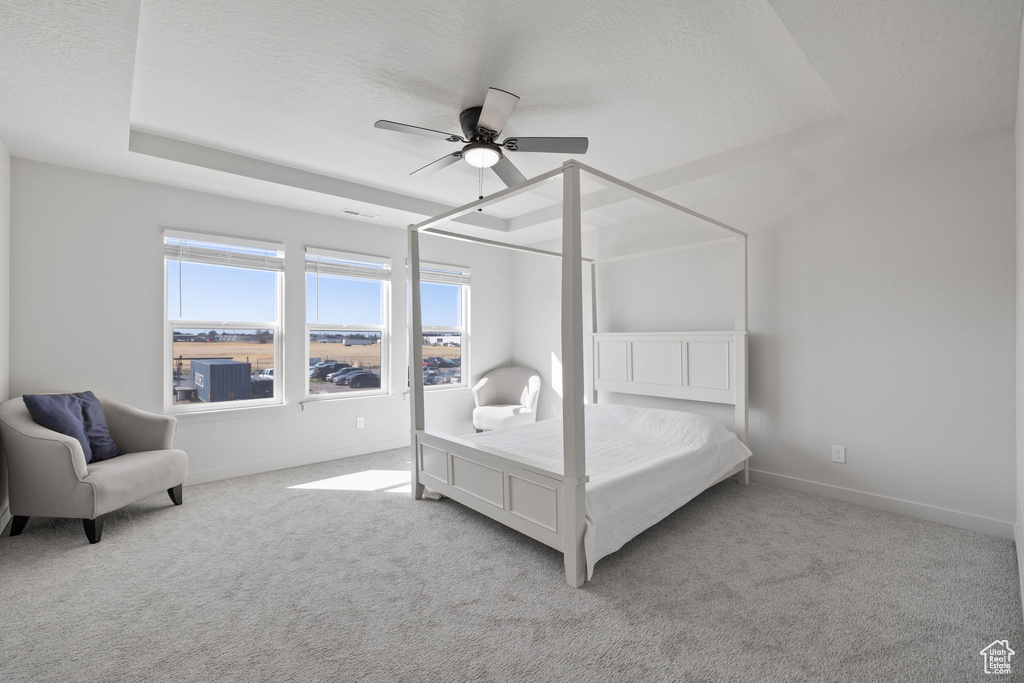 Bedroom featuring ceiling fan, light colored carpet, a textured ceiling, and a raised ceiling