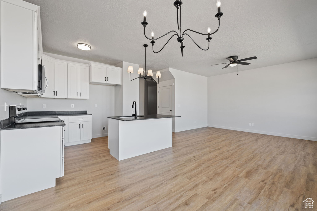 Kitchen with white cabinets, hanging light fixtures, a textured ceiling, a center island with sink, and light hardwood / wood-style flooring