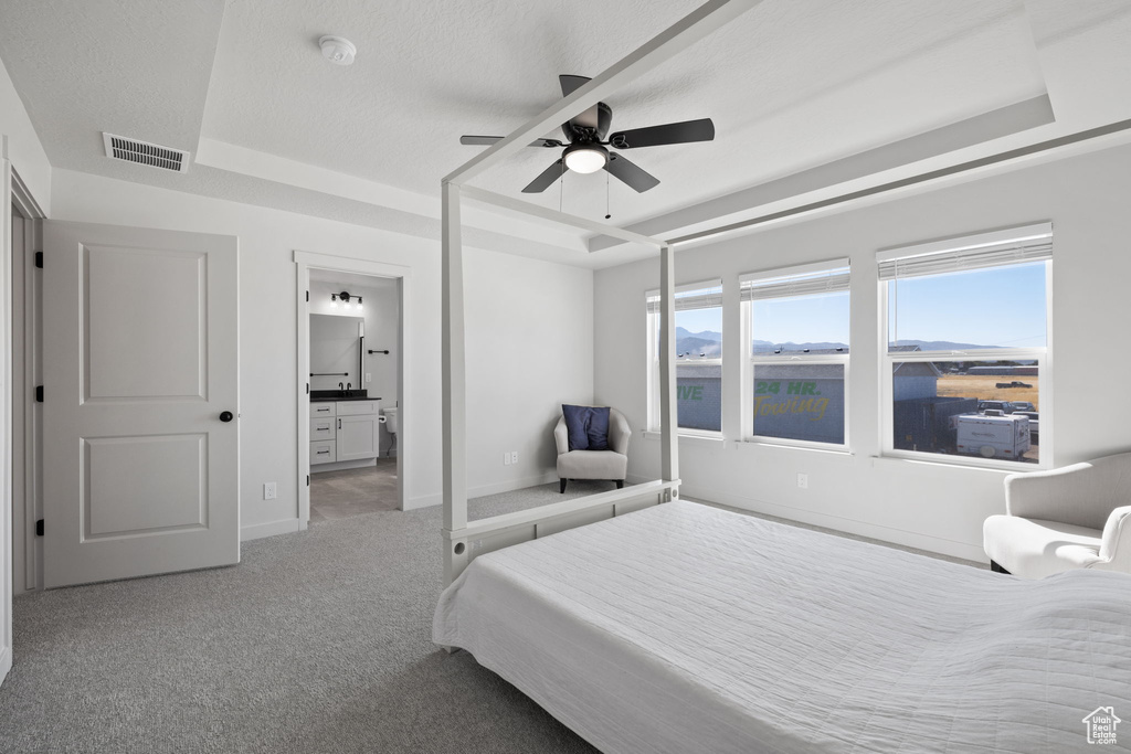 Bedroom with a raised ceiling, connected bathroom, ceiling fan, and light colored carpet