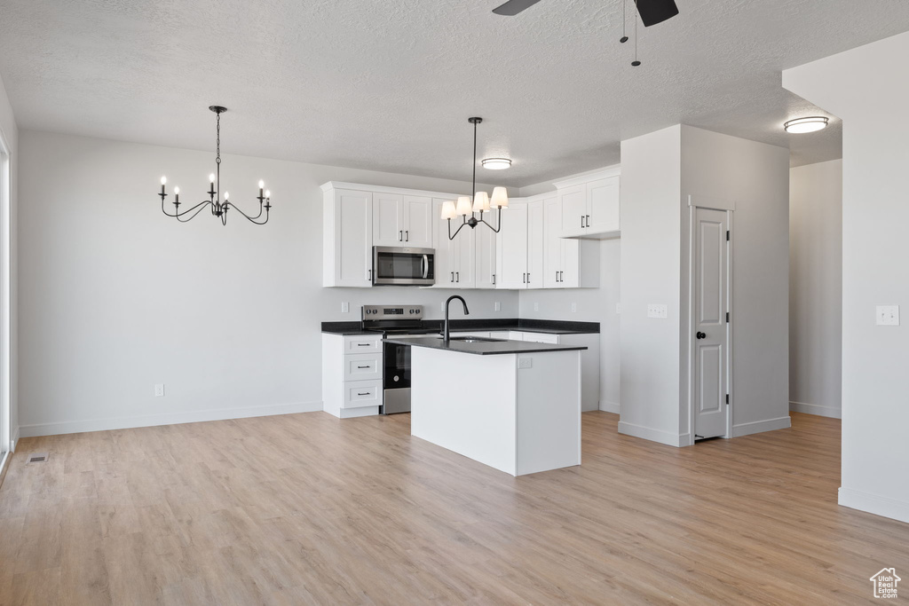 Kitchen featuring appliances with stainless steel finishes, hanging light fixtures, a center island with sink, and white cabinetry