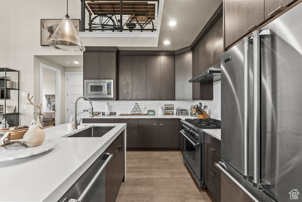 Kitchen with high end appliances, decorative light fixtures, light wood-type flooring, dark brown cabinets, and sink