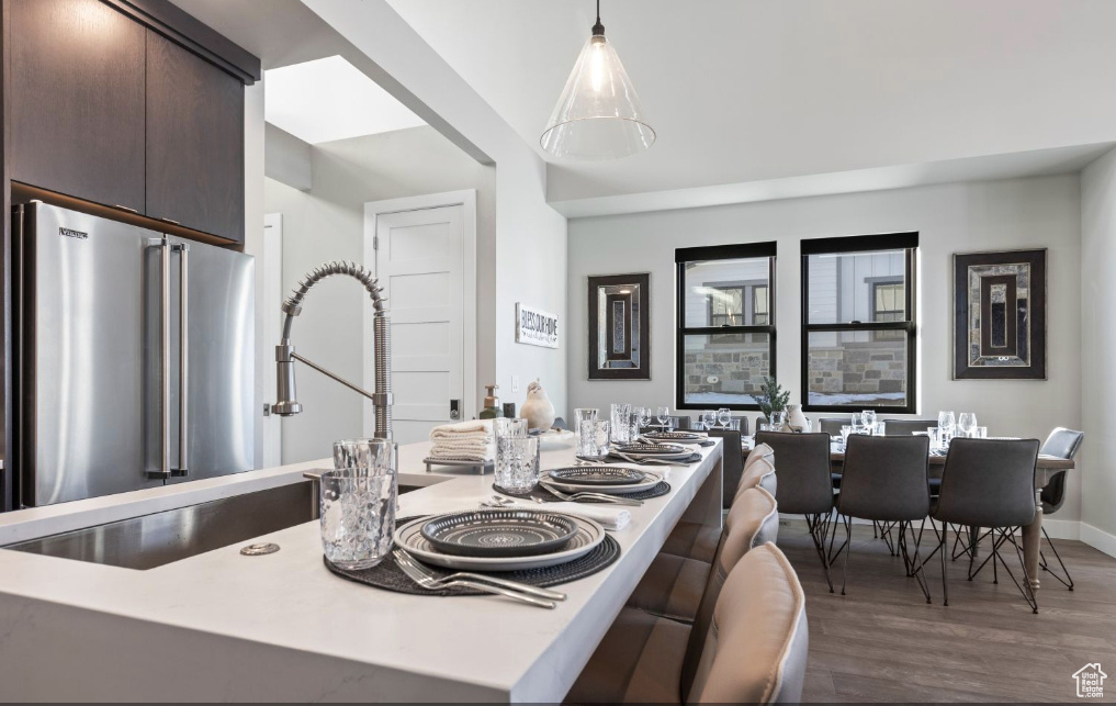 Interior space with hardwood / wood-style flooring, high end fridge, dark brown cabinets, and hanging light fixtures