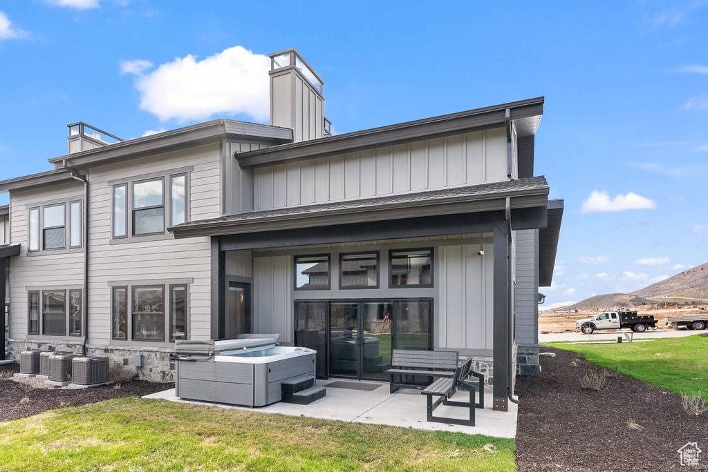 Rear view of property featuring a patio area, a mountain view, central AC unit, a hot tub, and a lawn