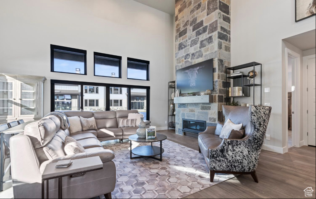 Living room featuring a towering ceiling, hardwood / wood-style flooring, and a stone fireplace