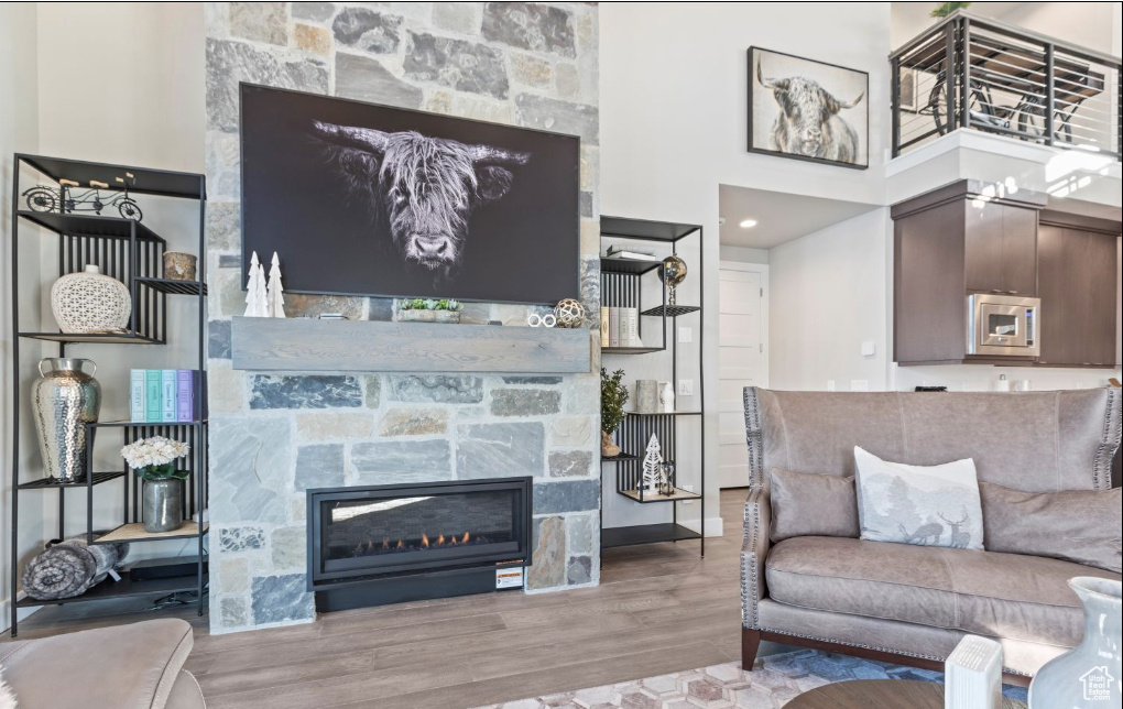 Living room with hardwood / wood-style floors, a high ceiling, and a stone fireplace