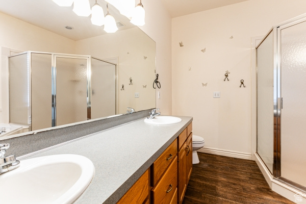 Full bathroom featuring independent shower and bath, vanity with extensive cabinet space, dual sinks, toilet, and hardwood / wood-style flooring