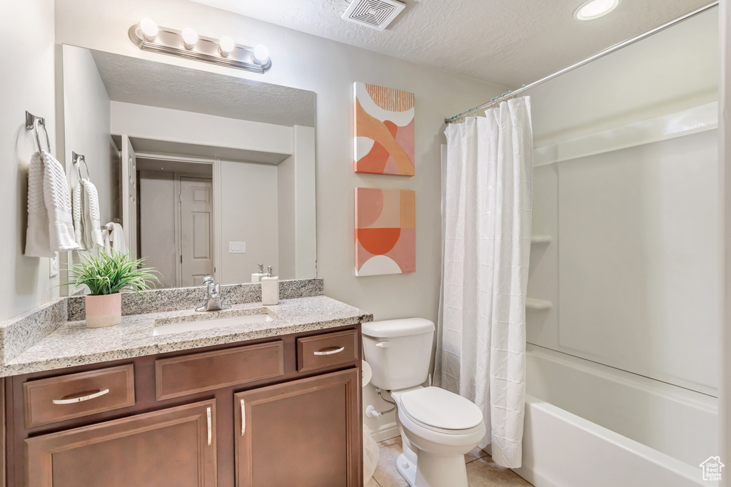 Full bathroom featuring shower / bath combination with curtain, toilet, tile flooring, a textured ceiling, and vanity