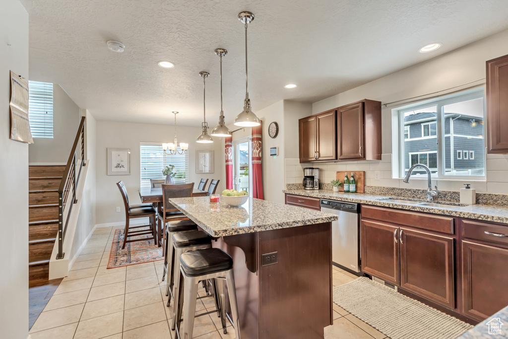 Kitchen with decorative light fixtures, a kitchen island, backsplash, light tile flooring, and dishwasher