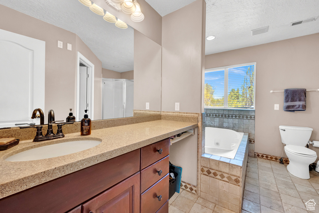 Bathroom with toilet, vanity with extensive cabinet space, tile flooring, a textured ceiling, and tiled bath