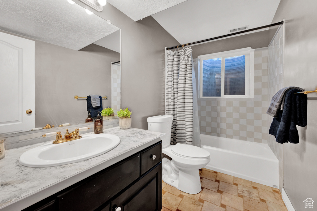 Full bathroom featuring a textured ceiling, shower / bath combo, tile floors, toilet, and vanity