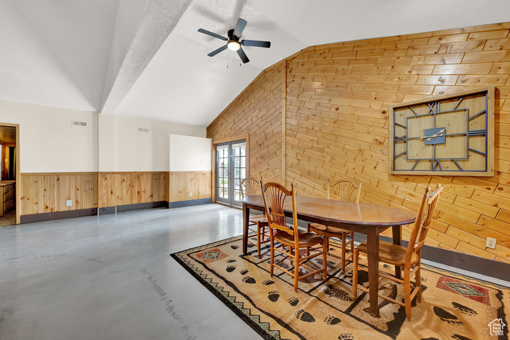 Dining room featuring wood walls, ceiling fan, concrete floors, and vaulted ceiling