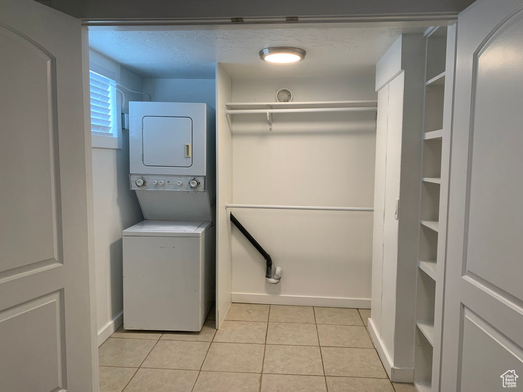 Clothes washing area with light tile floors and stacked washer / dryer