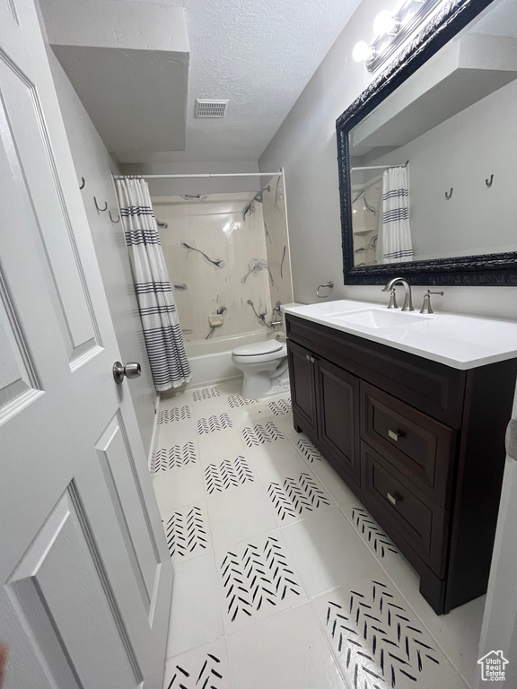 Full bathroom with a textured ceiling, tile patterned floors, shower / tub combo with curtain, vanity, and toilet