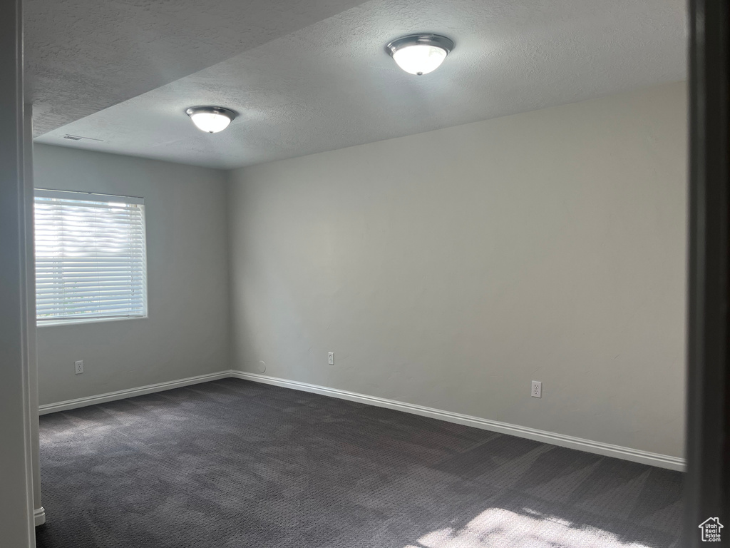 Spare room featuring a textured ceiling and dark carpet