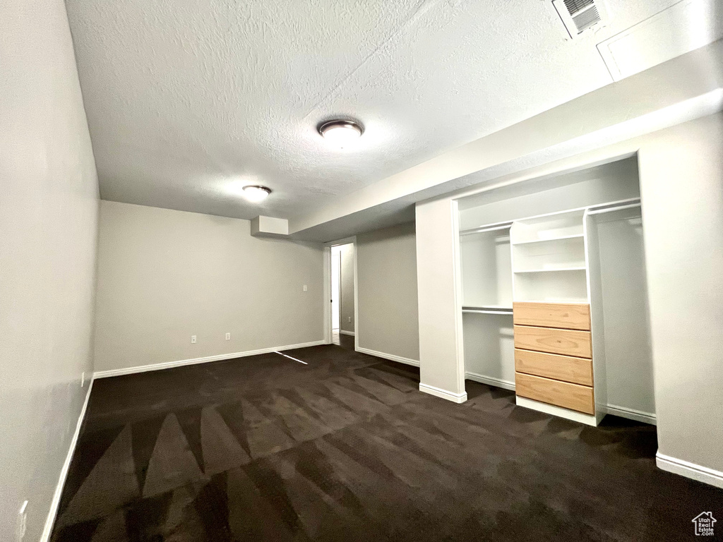 Basement with dark colored carpet and a textured ceiling