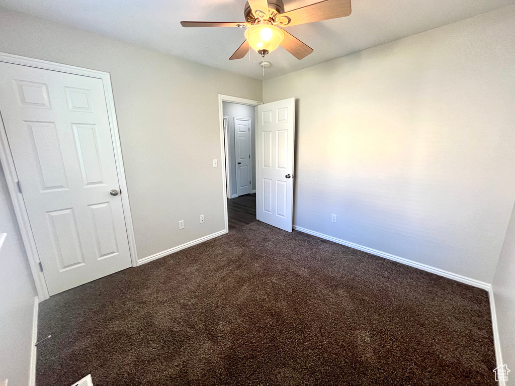 Unfurnished bedroom featuring dark colored carpet and ceiling fan