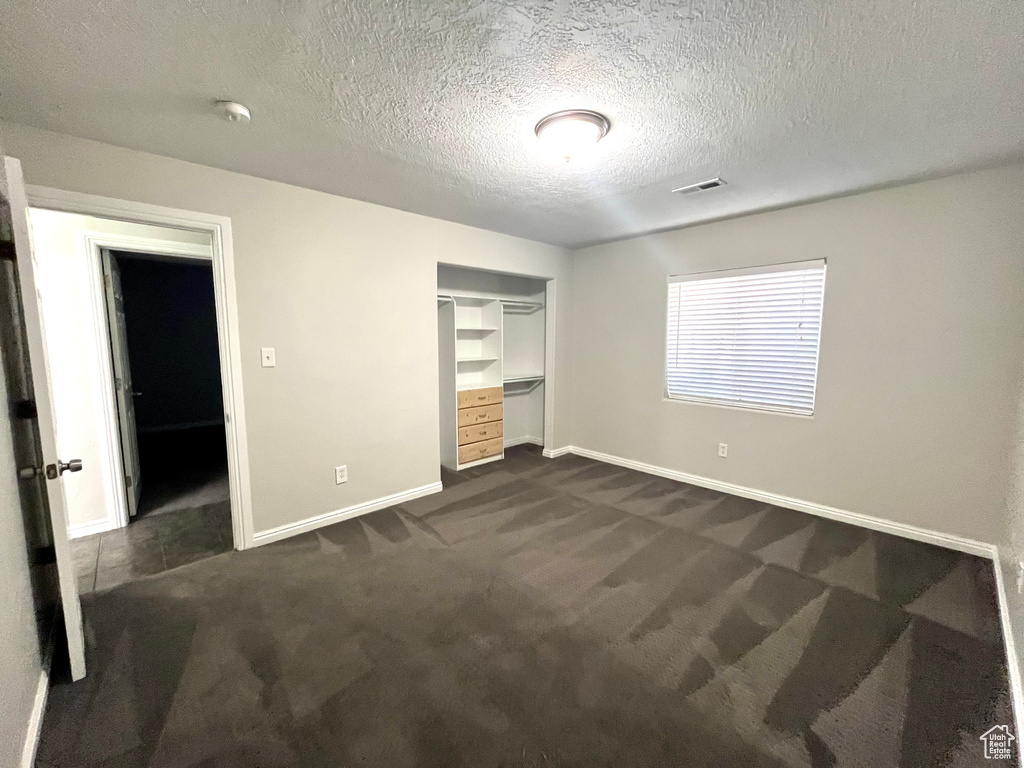 Unfurnished bedroom with built in desk, dark colored carpet, a closet, a textured ceiling, and a walk in closet