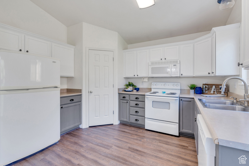 Kitchen with sink, white appliances, lofted ceiling, and hardwood / wood-style flooring