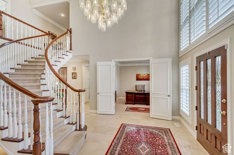 Entrance foyer with a notable chandelier, a high ceiling, light tile flooring, and crown molding