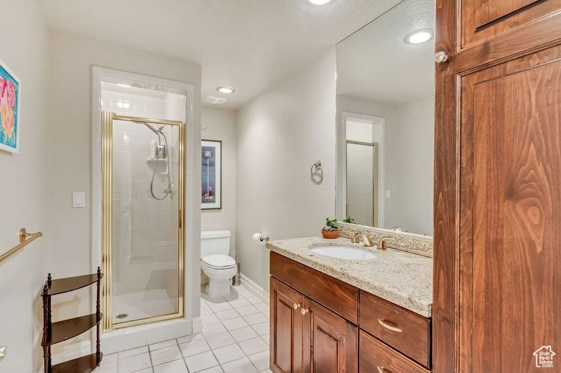 Bathroom featuring a shower with shower door, toilet, oversized vanity, and tile flooring
