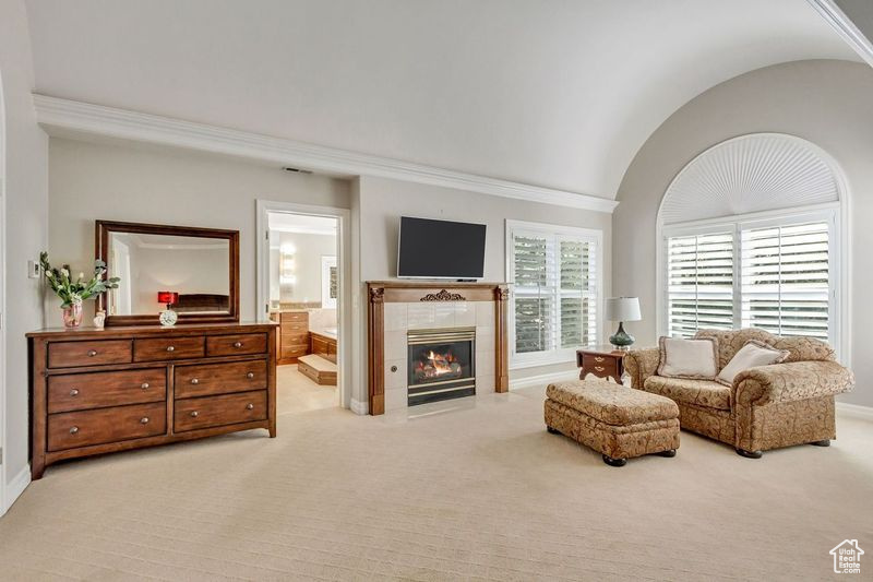 Carpeted living room with ornamental molding, a tiled fireplace, and vaulted ceiling