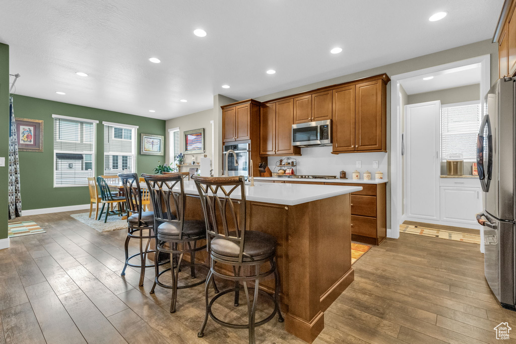 Kitchen featuring hardwood / wood-style flooring, a healthy amount of sunlight, appliances with stainless steel finishes, and an island with sink