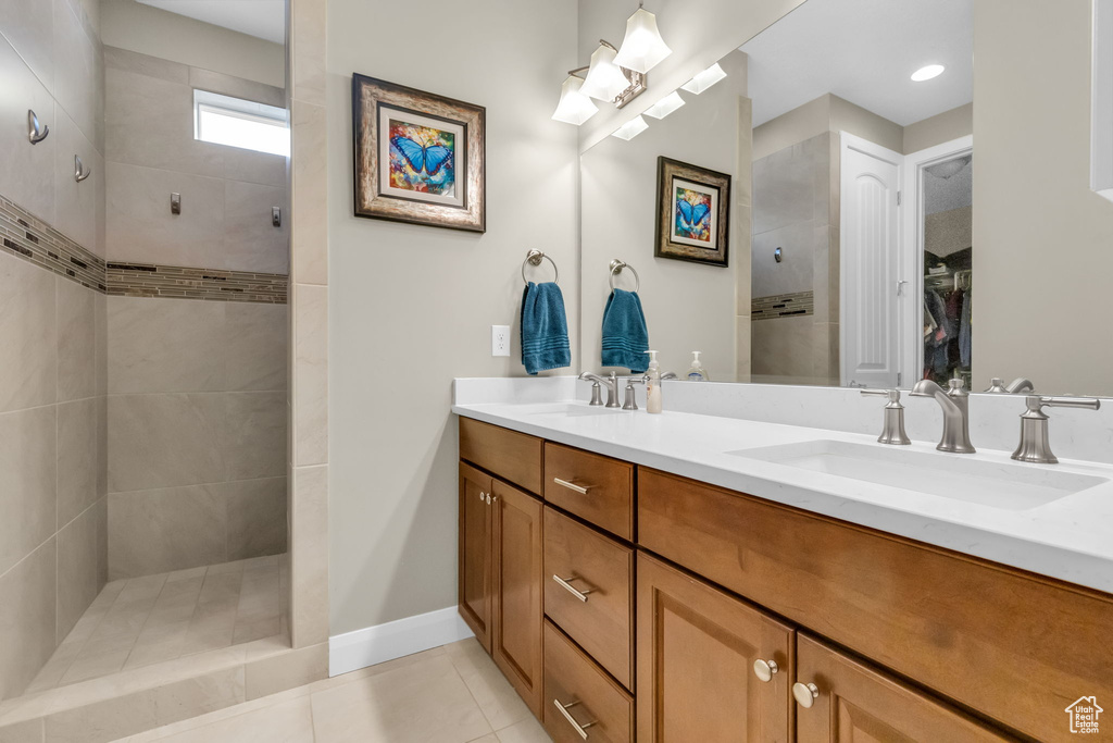 Bathroom featuring tile flooring, large vanity, tiled shower, and dual sinks