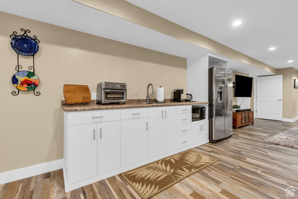 Kitchen featuring white cabinets, sink, light hardwood / wood-style floors, black microwave, and stainless steel fridge