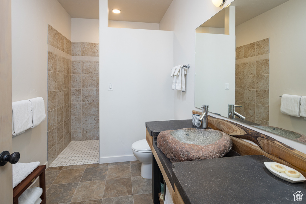 Bathroom with tiled shower, vanity, toilet, and tile floors