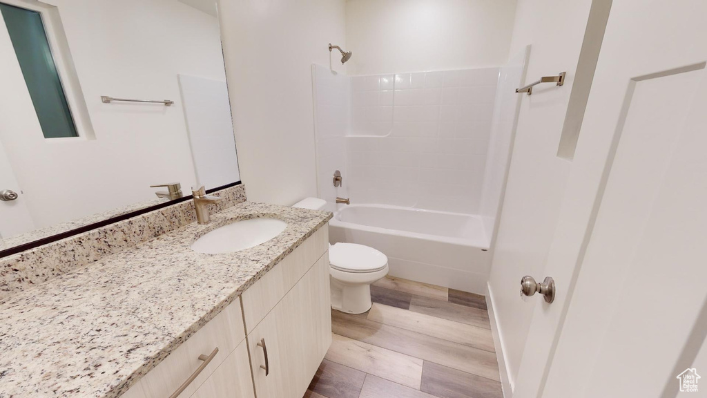 Full bathroom featuring washtub / shower combination, toilet, vanity with extensive cabinet space, and hardwood / wood-style flooring