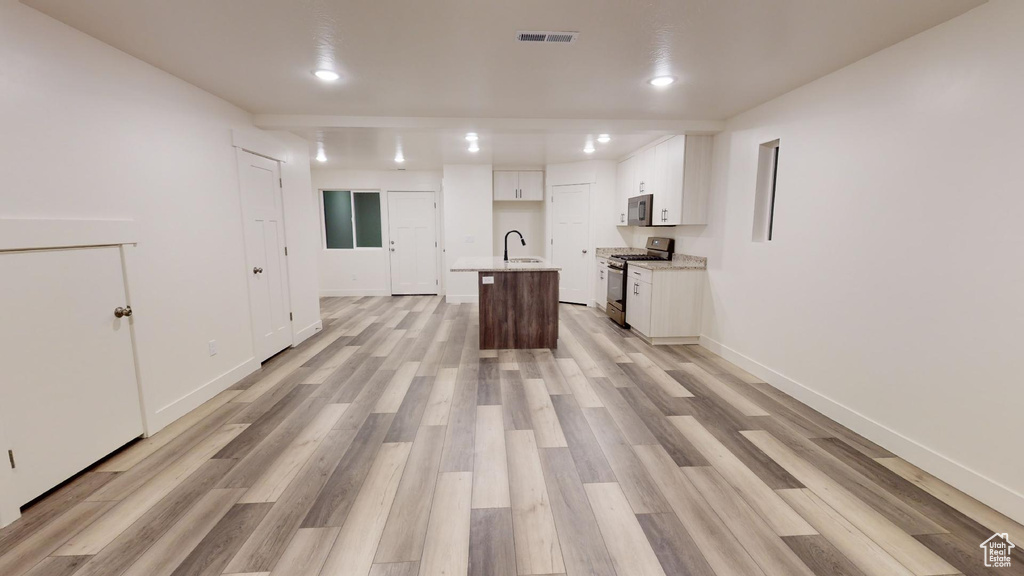 Kitchen with a center island with sink, light hardwood / wood-style floors, stove, white cabinetry, and sink