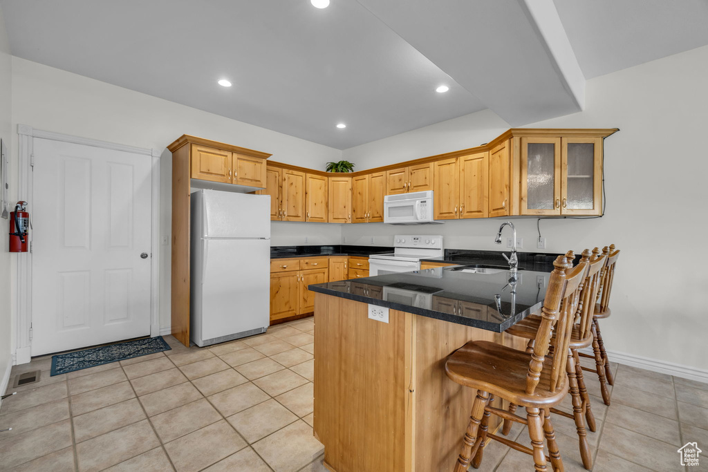 Kitchen with a breakfast bar, sink, white appliances, light tile flooring, and kitchen peninsula